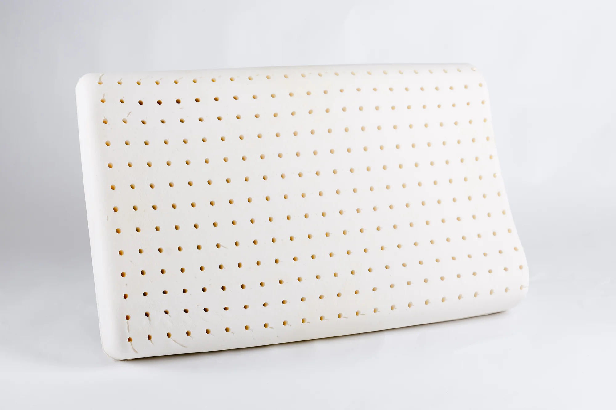 Natural latex pillow shown at an angle with visible perforation holes